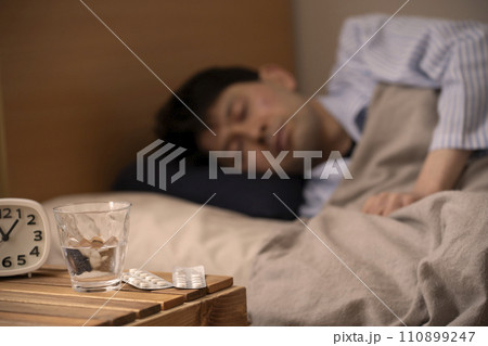睡眠薬　不眠症　薬を飲んで眠る男性　 110899247
