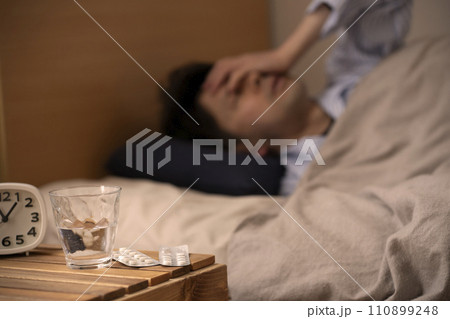 睡眠薬　不眠症　薬を飲んで眠る男性　 110899248
