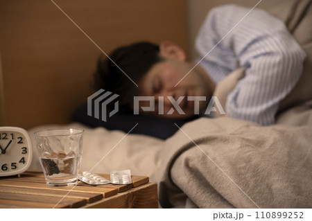 睡眠薬　不眠症　薬を飲んで眠る男性　 110899252