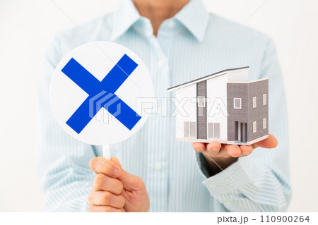 住宅模型とバツサインのプレートを持つミドル女性 住宅模型とバツサインのプレートを持つミドル女性 110900264