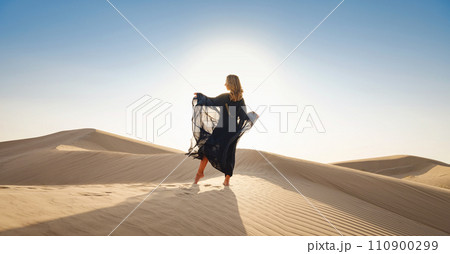Desert adventure. Young arabian Woman posing in traditional Emirati dress abaya in sanddunes of UAE desert at sunset. The Dubai Desert Conservation Reserve, United Arab Emirates. 110900299