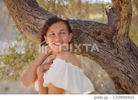 Beautiful Asian young woman in white dress outdoor near olive tree. embracing fresh air and engaging in outdoor activities. Friluftsliv concept means spending as much time outdoors as possible 110900845