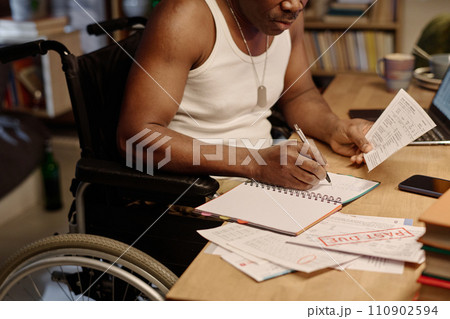 Unrecognizable black man in wheelchair writing information from piece of paper into his notebook 110902594