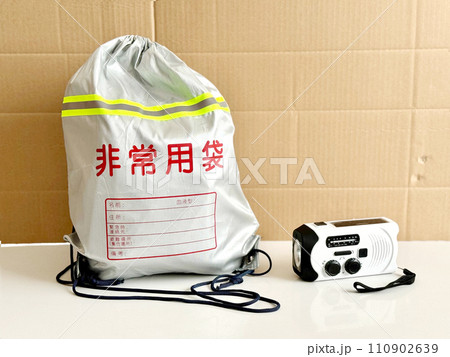 非常用袋とラジオ付き懐中電灯_段ボール背景 110902639