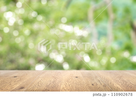 木目のある木製のテーブル越しに見えるボケた背景、奥行きのある背景、緑の植物の背景画像 110902678