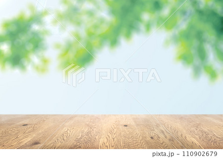 木目のある木製のテーブル越しに見えるボケた背景、奥行きのある背景、木の葉っぱと空の背景画像 110902679