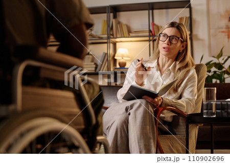 Professional psychologist sitting in armchair at her office and talking to unrecognizable patient Professional psychologist sitting in armchair at her office and talking to unrecognizable patient 110902696