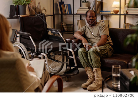 Black veteran with disability sitting on couch in relaxed pose and talking to therapist taking notes 110902700