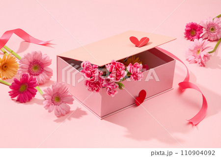 On a pink background, a pink gift box decorated with fresh flower, gerbera and carnation. Creative ideas for decorate on women day. Advertising photo 110904092