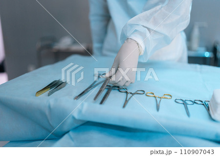 Close-up cropped shot of unrecognizable surgeon taking surgical scissors from operating table during operation. Closeup of scrub nurse taking medical instruments for operation. Concept of emergency. Close-up cropped shot of unrecognizable surgeon taking surgical scissors from operating table during operation. Closeup of scrub nurse taking medical instruments for operation. Concept of emergency. 110907043