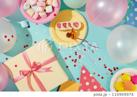 Balloons are decorated around the frame. A gift box, a plate of marshmallows, a plate of macarons and a plate of cakes are displayed on a blue background with confetti. Balloons are decorated around the frame. A gift box, a plate of marshmallows, a plate of macarons and a plate of cakes are displayed on a blue background with confetti. 110909978