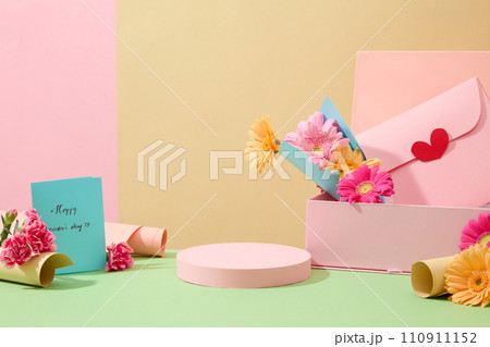 Front view of a pastel pink podium for product display, surrounded by greeting cards, gift boxes, gift wrap and fresh flowers. Background with pastel colors. 110911152