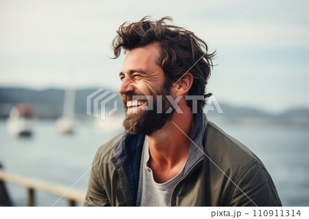 Portrait of a handsome man laughing on a pier with a boat in the background. 110911314