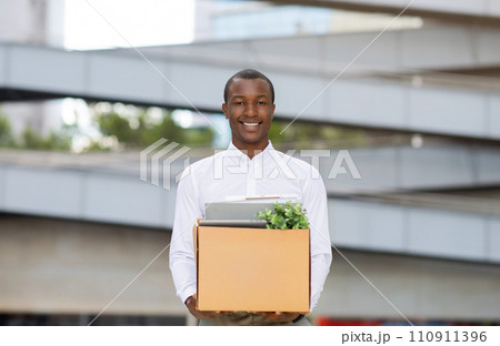 Happy black man in white shirt posing outdoors with box of belongings 110911396