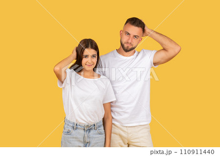 Pensive sad confused young european man and lady in white t-shirts scratches head 110911440
