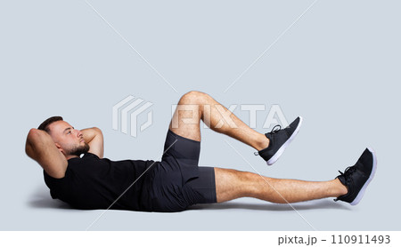 Concentrated handsome strong young caucasian guy with beard in sportswear make exercises for legs and abs Concentrated handsome strong young caucasian guy with beard in sportswear make exercises for legs and abs 110911493
