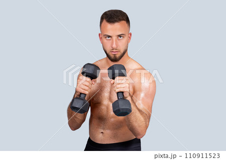 Serious sweat muscular young caucasian man athlete with beard, naked torso make exercises with dumbbell for hands 110911523