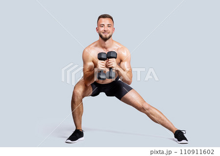 Smiling sweat strong muscular young european man with beard, naked torso make exercises with dumbbells 110911602