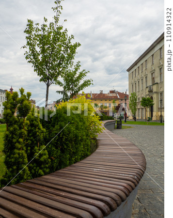 Curved wooden bench on city sidewalk next to vibrant green grass Curved wooden bench on city sidewalk next to vibrant green grass 110914322