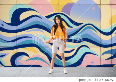 Young female graffiti painter standing near the wall with her paintings Young female graffiti painter standing near the wall with her paintings 110916675