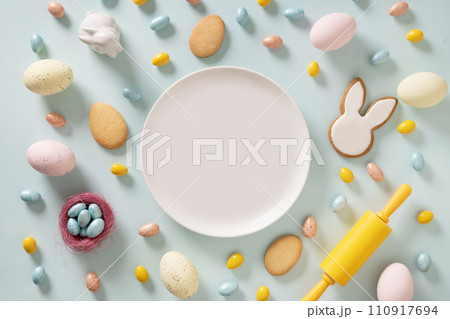 Easter homemade cookies shaped of bunny, sprinkles and sweet chocolate eggs on blue background. Homemade cook for holiday. View from above. Copy space. 110917694