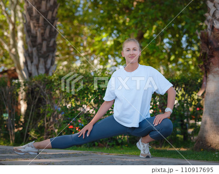 idea of healthy lifestyle and sports in a modern city. Female jogger. Fit young Caucasian woman stretching muscle in park before running and enjoying healthy outdoor. Fitness girl in public park. 110917695