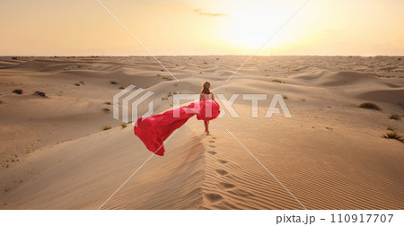Desert adventure. Young arabian Woman in red silk dress in sands dunes of UAE desert at sunset, fantastic view. The Dubai Desert Conservation Reserve, United Arab Emirates. 110917707