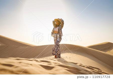Desert adventure. Young arabian Woman in zebra suits and hat in sands dunes of UAE desert at sunset. The Dubai Desert Conservation Reserve, United Arab Emirates. Desert adventure. Young arabian Woman in zebra suits and hat in sands dunes of UAE desert at sunset. The Dubai Desert Conservation Reserve, United Arab Emirates. 110917728