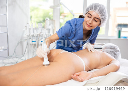 Young female cosmetologist performing ultrasound procedure on buttocks of young woman Young female cosmetologist performing ultrasound procedure on buttocks of young woman 110919469