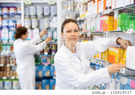 Adult female pharmacist arranges products in pharmacy 110919537