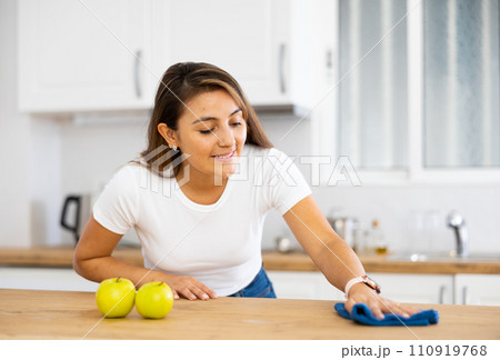 Smiling young Hispanic woman wiping kitchen surfaces at home 110919768