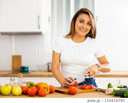 Positive young latin american girl cooking salad in home kitchen 110919795