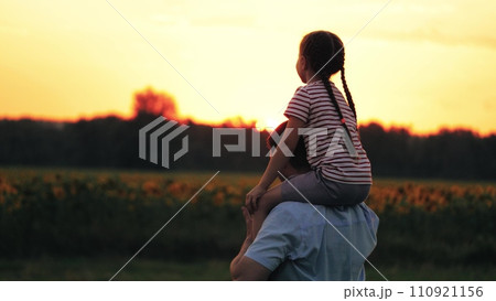 Daughter perches on shoulders of father pointing to sunset and dad follows gaze Daughter perches on shoulders of father pointing to sunset and dad follows gaze 110921156