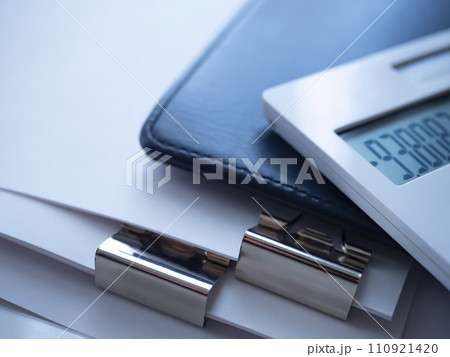テーブルに置かれた手帳と書類と電卓 110921420