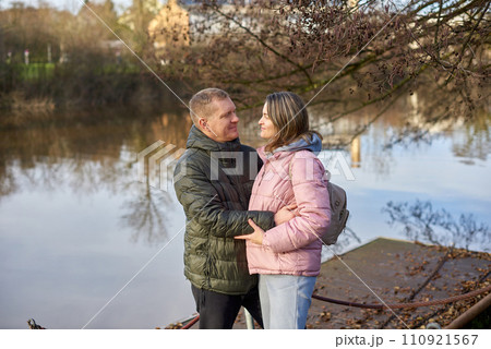 Loving couple on the shore of the pond in the park in autumn. A man and a woman. A couple, lovers on the shore of the lake on a walk. Autumn Romance by the Lake: Happy Couple's Lakeside Leisure Loving couple on the shore of the pond in the park in autumn. A man and a woman. A couple, lovers on the shore of the lake on a walk. Autumn Romance by the Lake: Happy Couple's Lakeside Leisure 110921567