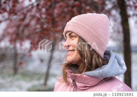 Winter Elegance: Portrait of a Beautiful Girl in a Snowy European Village. Winter lifestyle portrait of cheerful pretty girl. Smiling and having fun in the snow park. Snowflakes falling down 110921691