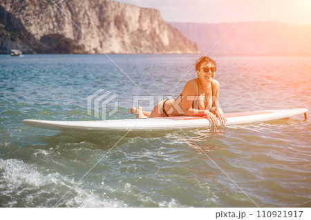 Woman sup sea travel. Sports girl on a surfboard in the sea on a sunny summer day. In a black bathing suit, he sits on a sapa in the sea. Rest on the sea. 110921917