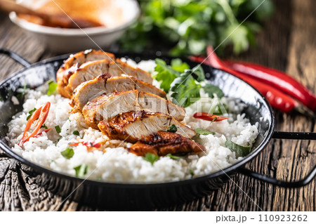 Grilled chicken breast served in a pan with jasmine rice and chili peppers Grilled chicken breast served in a pan with jasmine rice and chili peppers 110923262