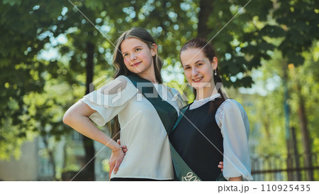 Two Russian schoolgirls graduate posing on a summer day. 110925435