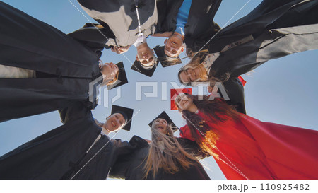 College graduates in a circle stand hugging each other. College graduates in a circle stand hugging each other. 110925482