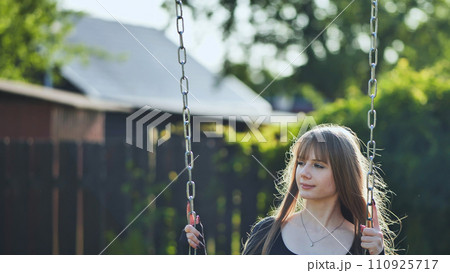 A blonde-haired girl in a black dress rides on a swing. 110925717
