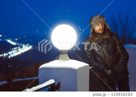 A man stands at a lantern at night in a hat with earflaps 110930283