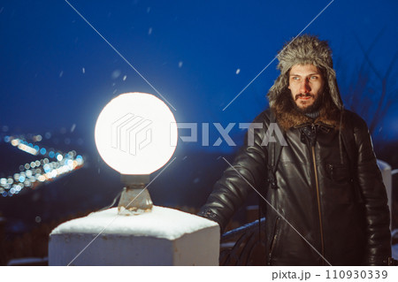 A man stands at a lantern at night in a hat with earflaps 110930339