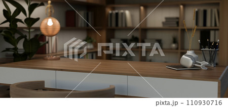 A copy space on a wooden desk and a large bookshelf in a modern home office at night. A copy space on a wooden desk and a large bookshelf in a modern home office at night. 110930716