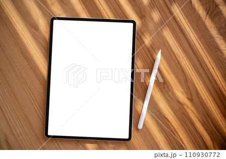 A wooden desk workspace with a white-screen digital tablet mockup and a tablet pen. 110930772