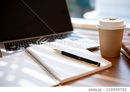 A wooden table with an opened book, a pen, a laptop, and a coffee cup. workspace in a cafe concept 110930782