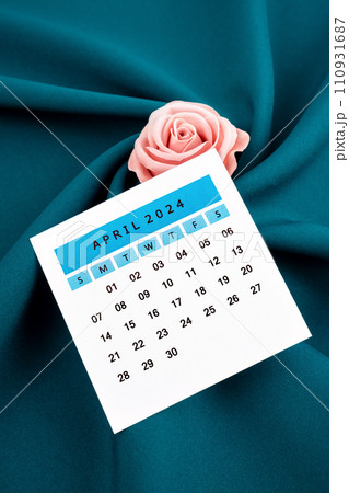 April 2024 calendar page and pink rose on green textile. 110931687