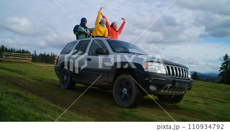 Hikers standing up through sunroof of car laugh and wave hands 110934792