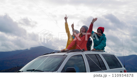 Hikers standing up through sunroof of car sing and dance 110934878