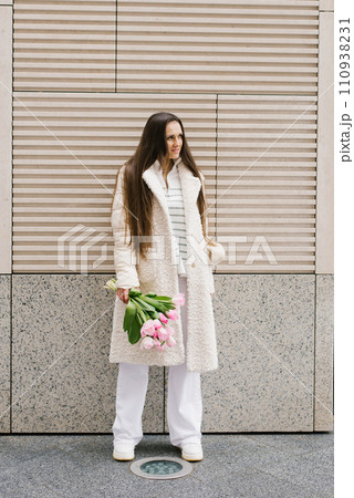 Young woman in stylish light coloured clothes strolls through the streets of the city with a bouquet of tulips 110938231